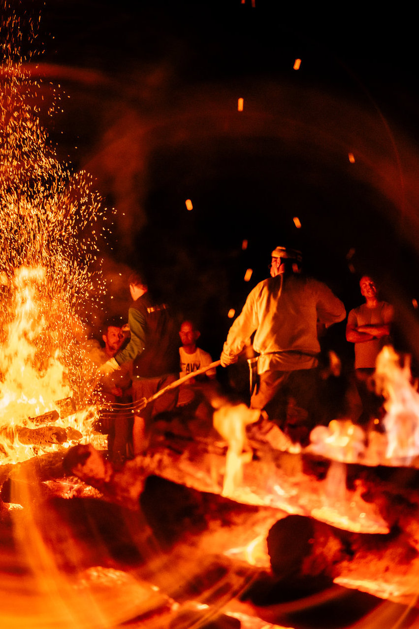 People tending a fire at night as sparks rise into the darkness