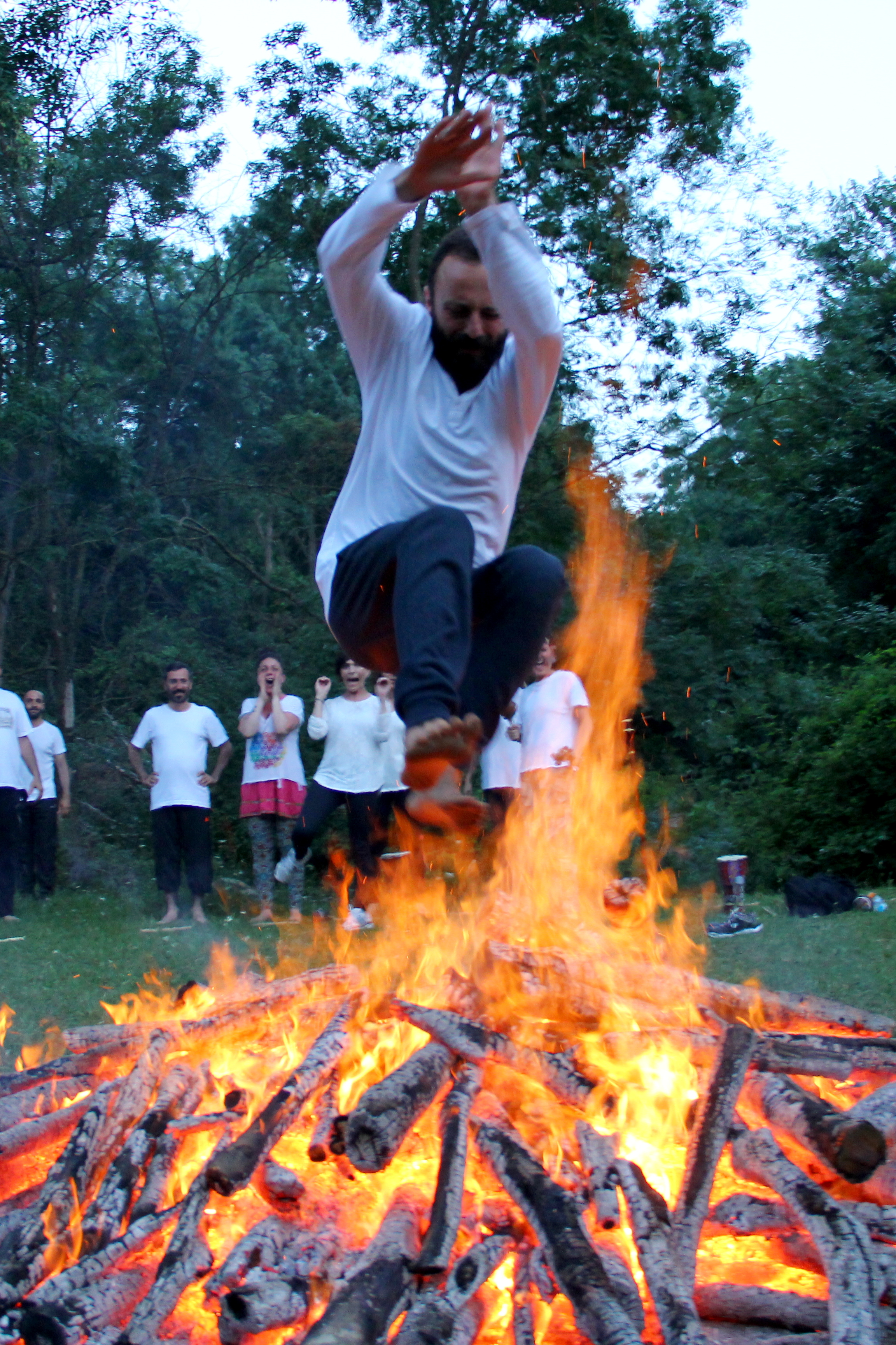 A participant leaping over the fire while the group watches