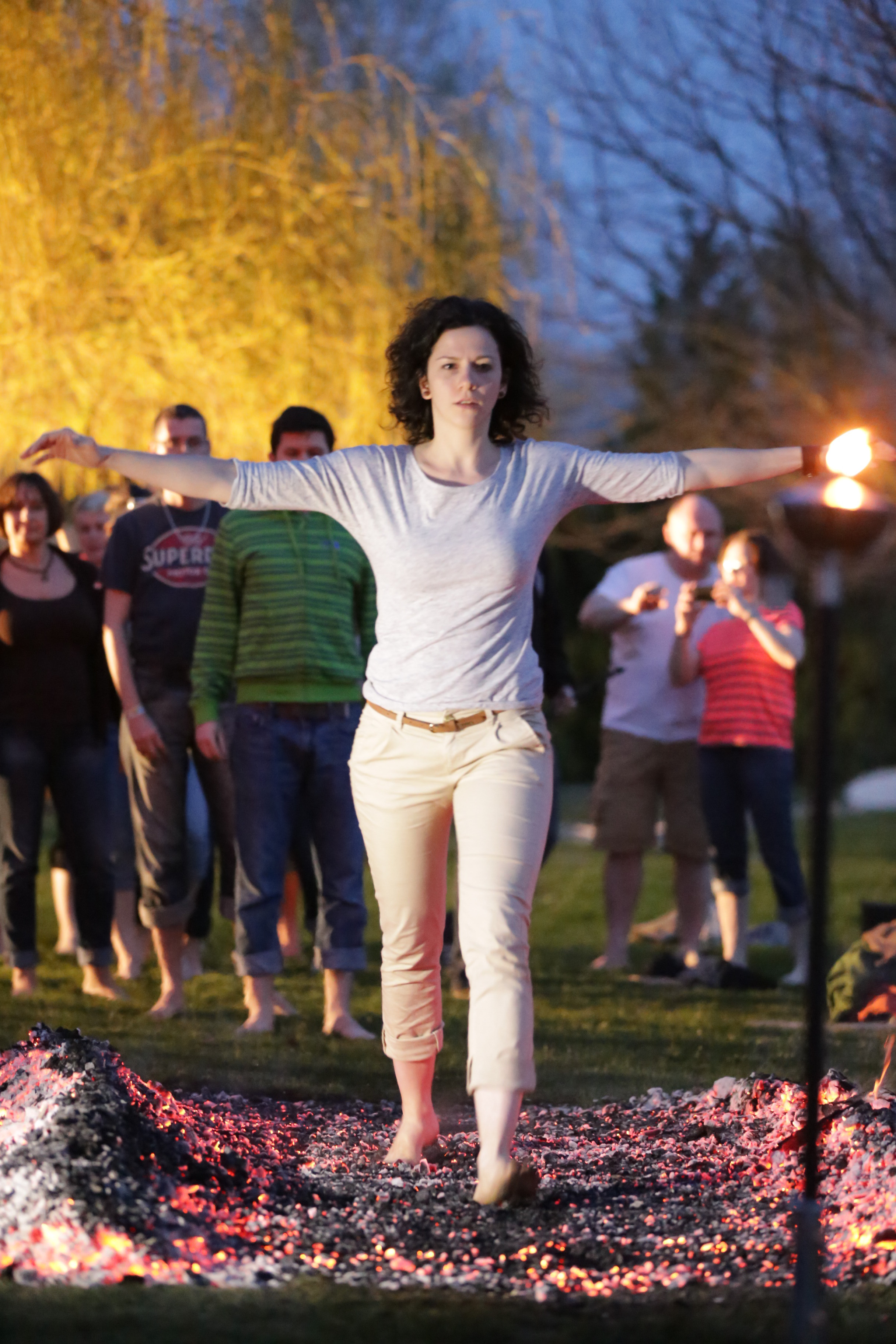 A woman crossing the embers with outstretched arms while colleagues witness and support