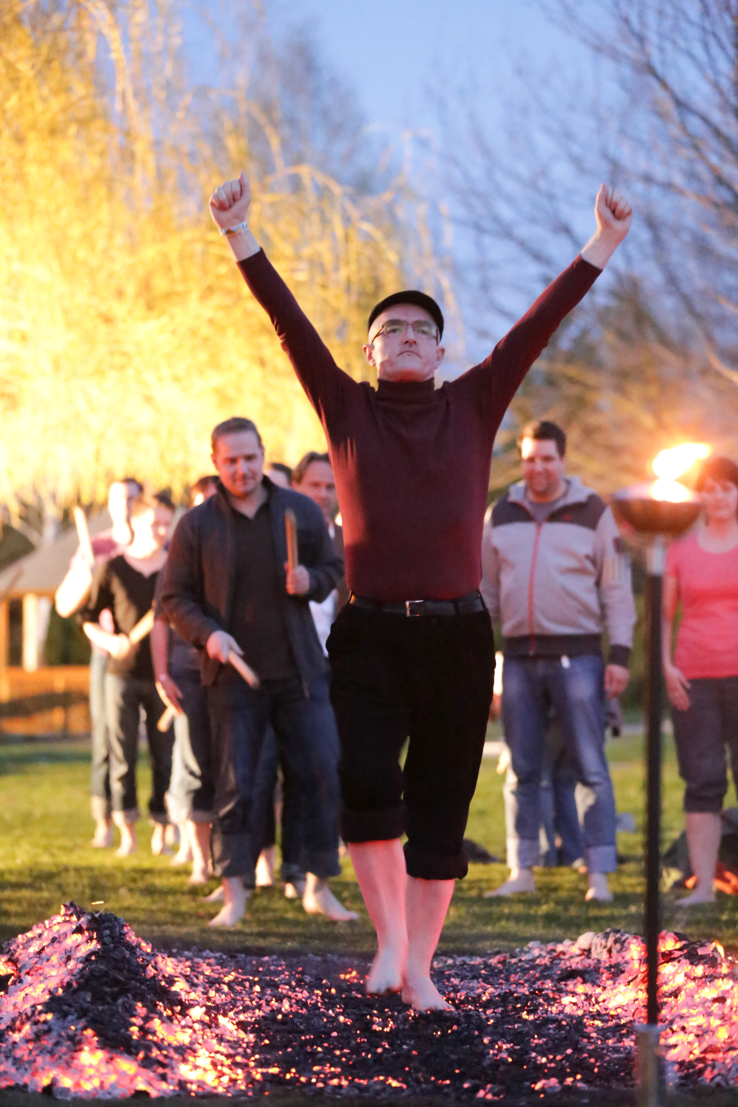 A participant in a hat crossing the embers with both arms raised