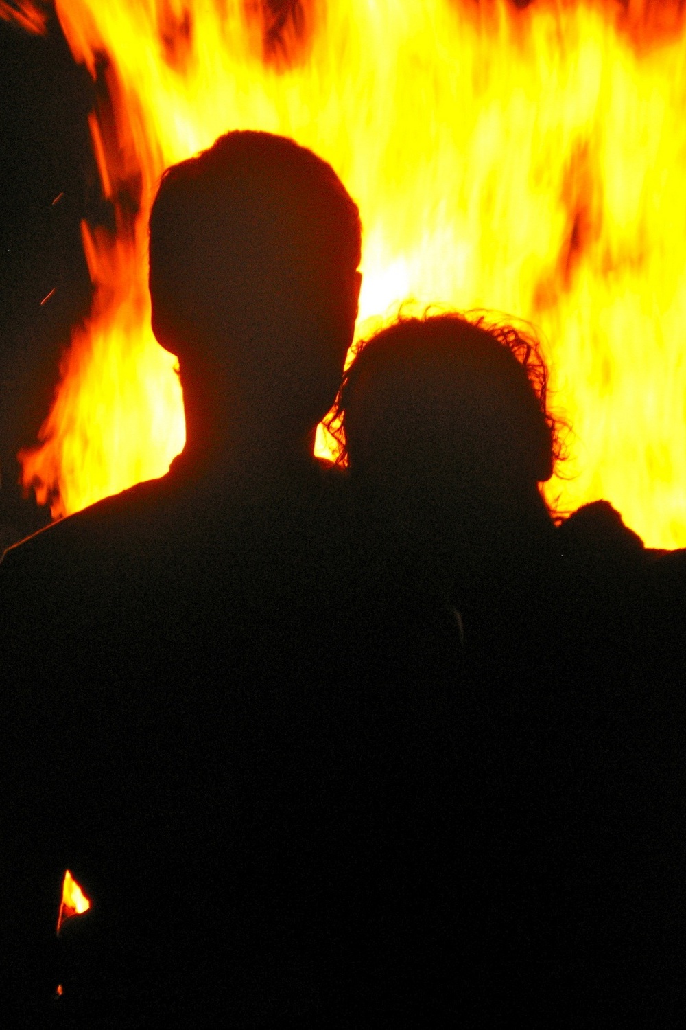 A couple seen in full silhouette while looking into a large fire