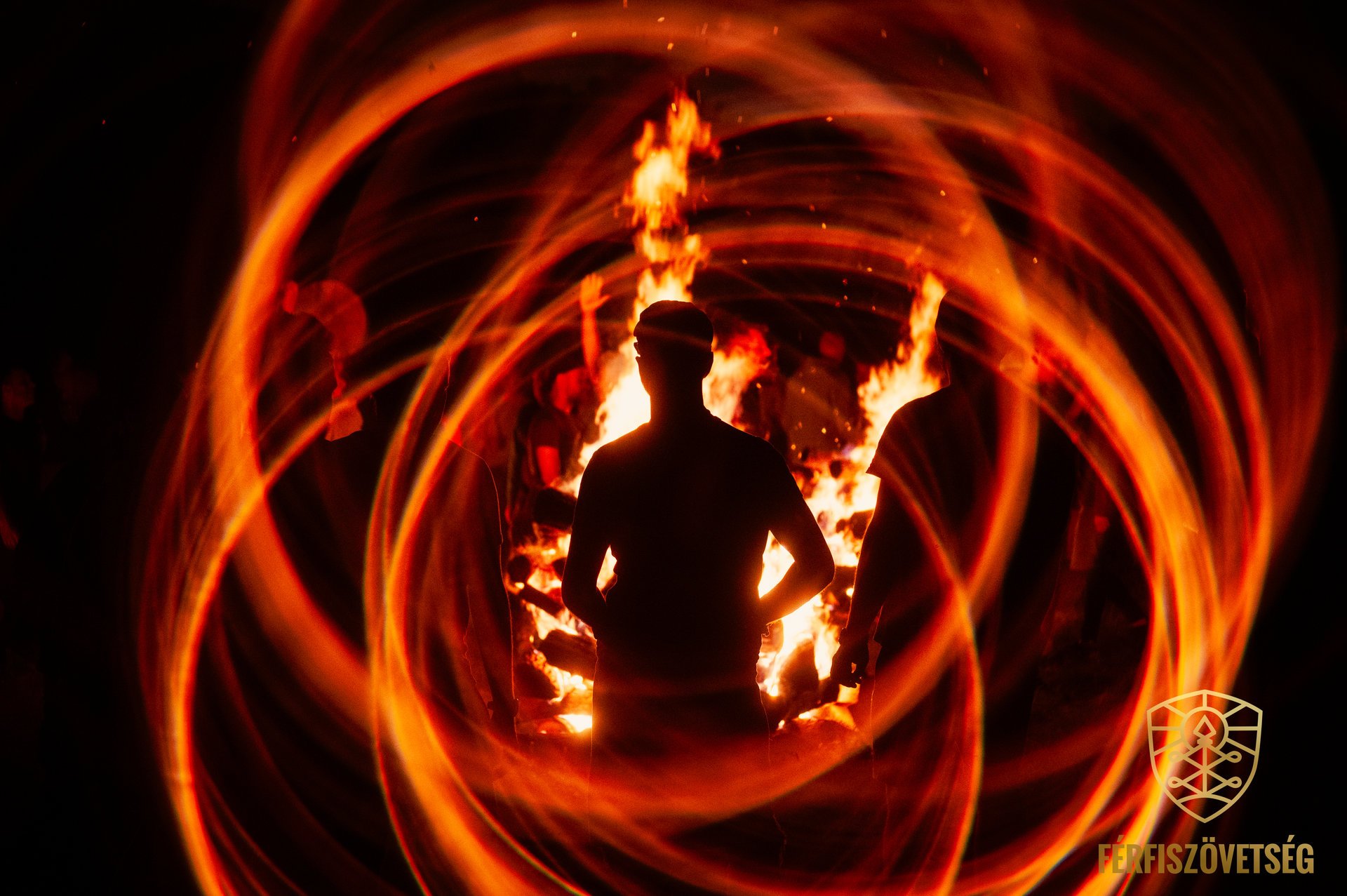 A human silhouette framed by a ceremonial fire and sweeping trails of light