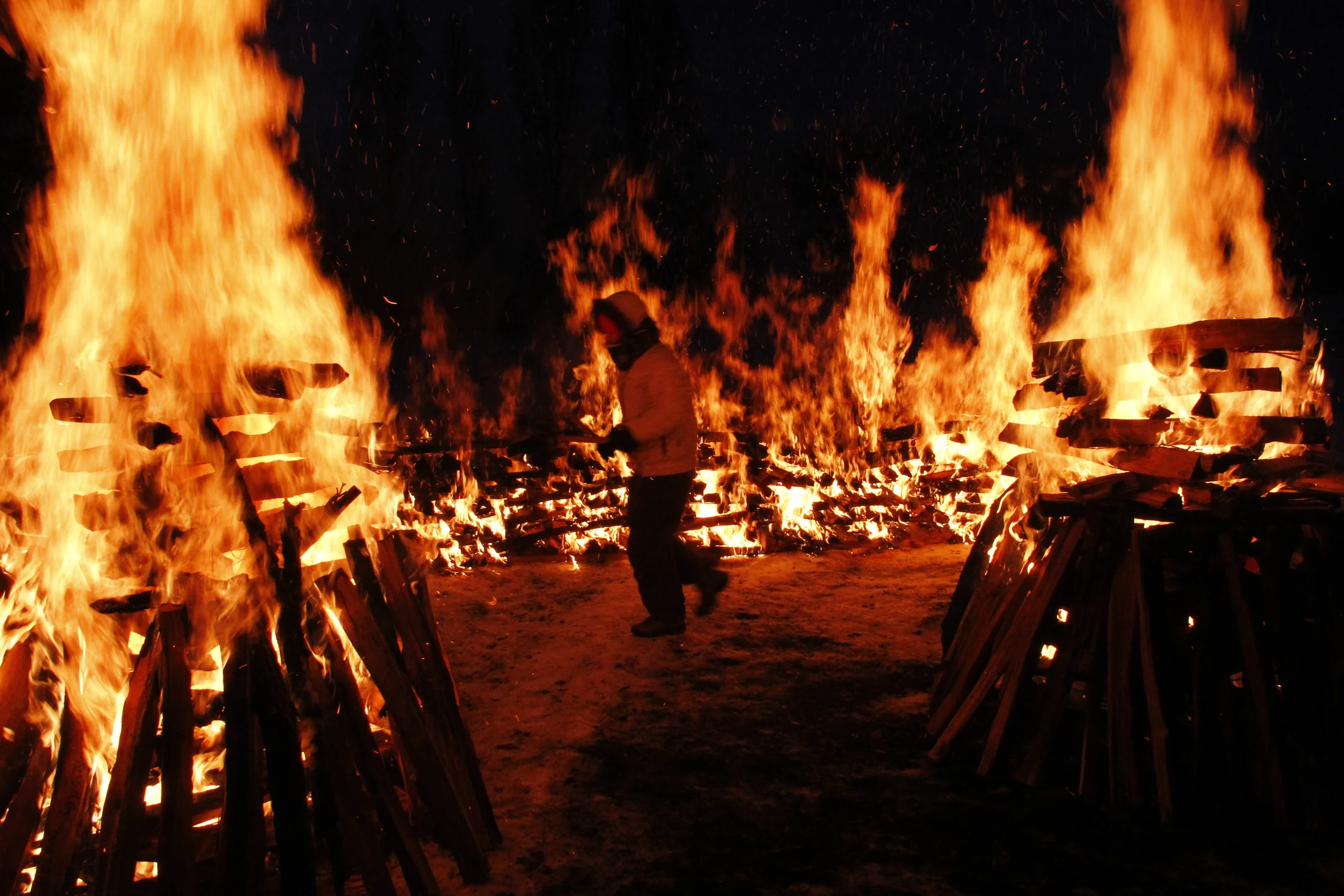 A woman in winter clothing walking between burning pyres