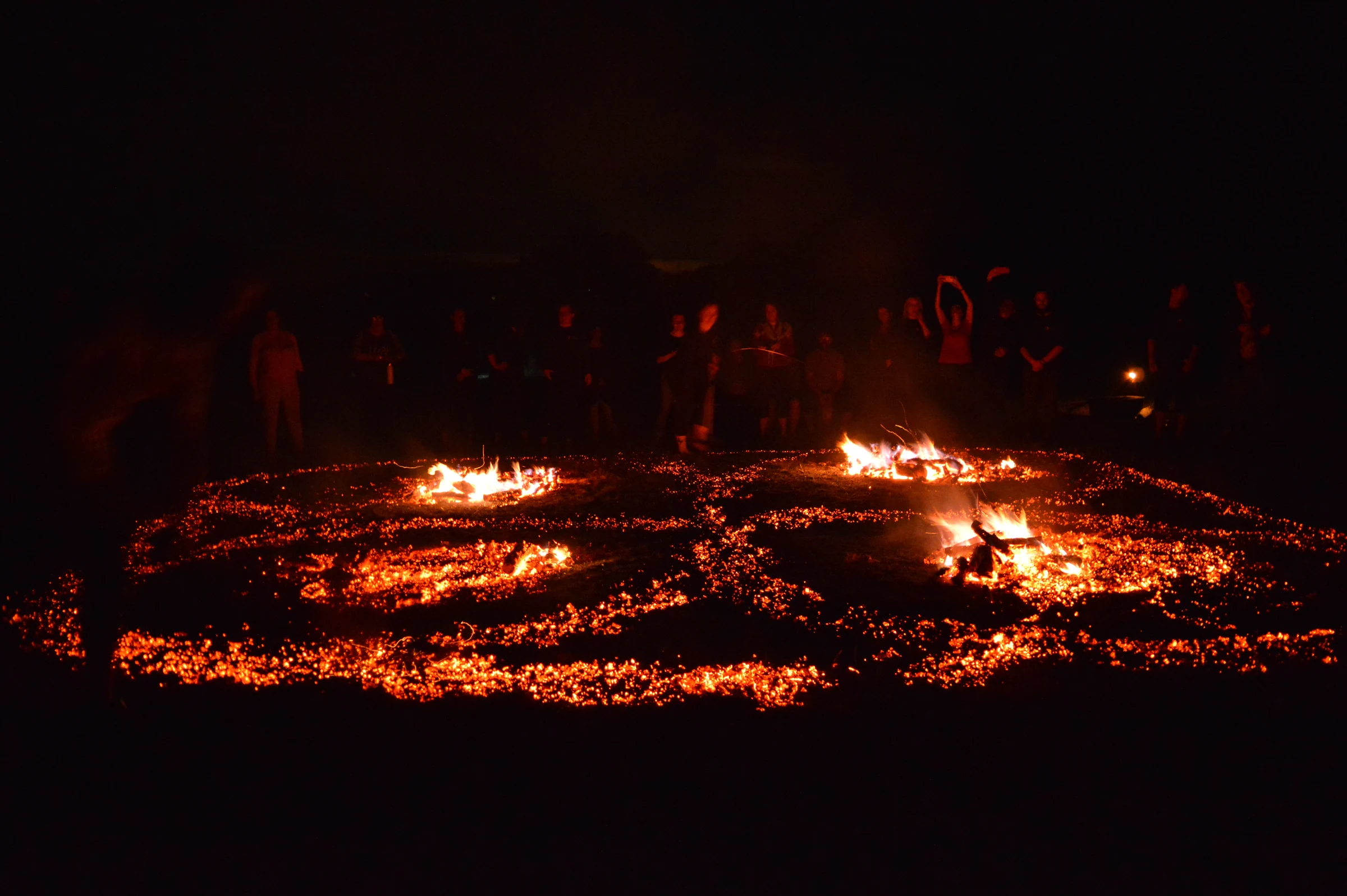 Concentric firewalking paths glowing in the darkness before a gathered group