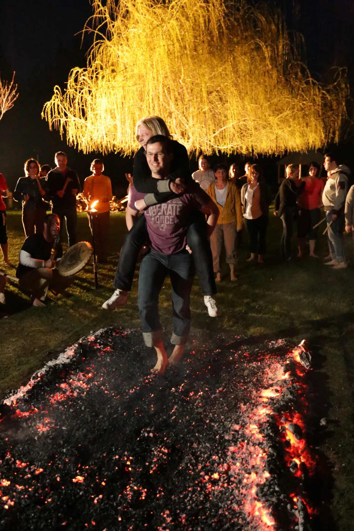 Two smiling participants crossing an ember bed together, one carrying the other